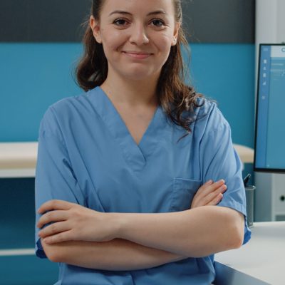 Portrait of medical assistant standing with arms crossed in cabinet for medical checkup visit. Woman nurse working with computer and documents in doctors office for healthcare system.